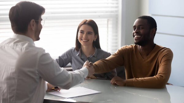Smiling african american satisfied client shaking hands with salesman.