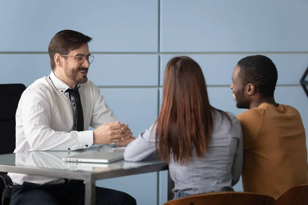 Multiracial clients meeting smiling bank worker at office.