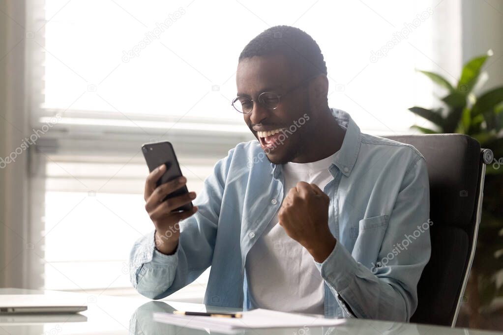 Euphoric millennial african american businessman looking at mobile phone screen.