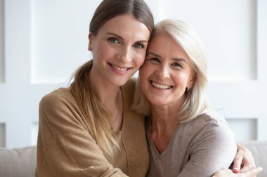 Çekici yaşlı anne ve yetişkin kız kameraya bakarak sarılıyorlar.