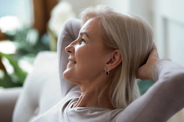 60s vrouw zet handen achter hoofd rusten binnen genieten weekend — Stockfoto