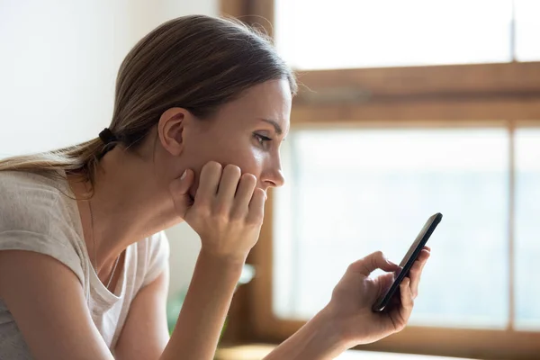 Nachdenklich traurige junge Frau hält Smartphone in der Hand und wartet auf SMS ihres Freundes — Stockfoto