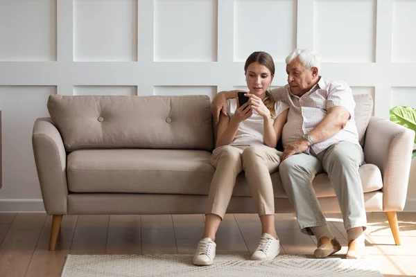 On one side of sofa sitting grandfather with adult granddaughter