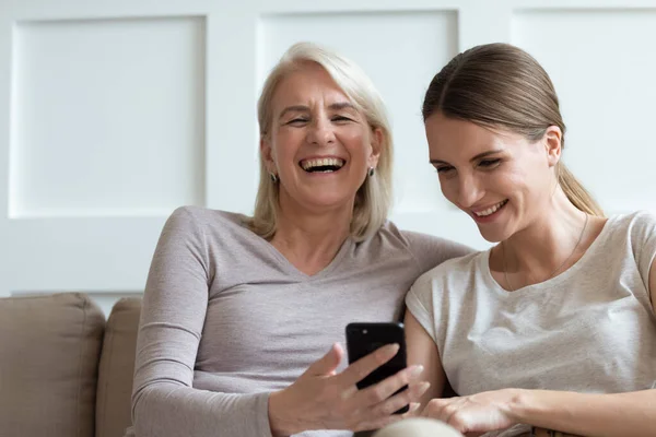 Мать и взрослая дочь смотрят смешные видео на смартфоне, смеясь — стоковое фото