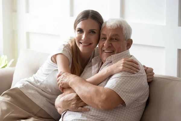 Adulto neta e avô idoso abraçando sentado no sofá dentro de casa — Fotografia de Stock