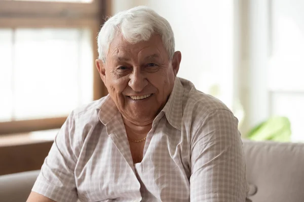 Пожилой человек, сидящий на диване, улыбается, глядя в камеру — стоковое фото