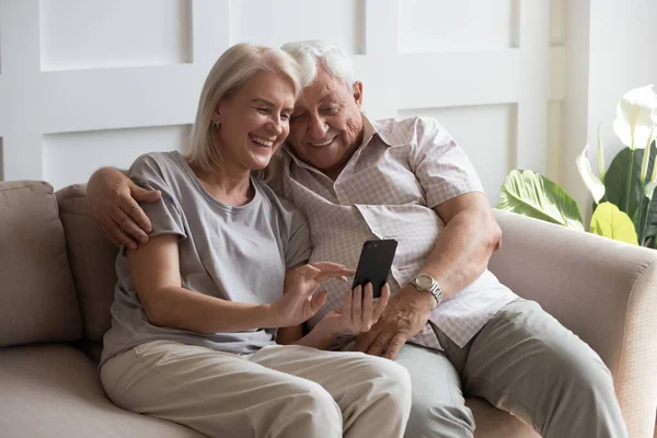 Elderly grandfather and grandmother spend time having fun using smartphone — Stock Photo, Image