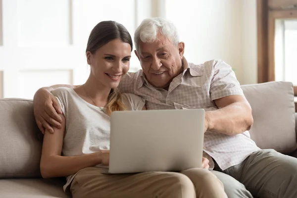 Дедушка и взрослая внучка сидят на диване с ноутбуком — стоковое фото