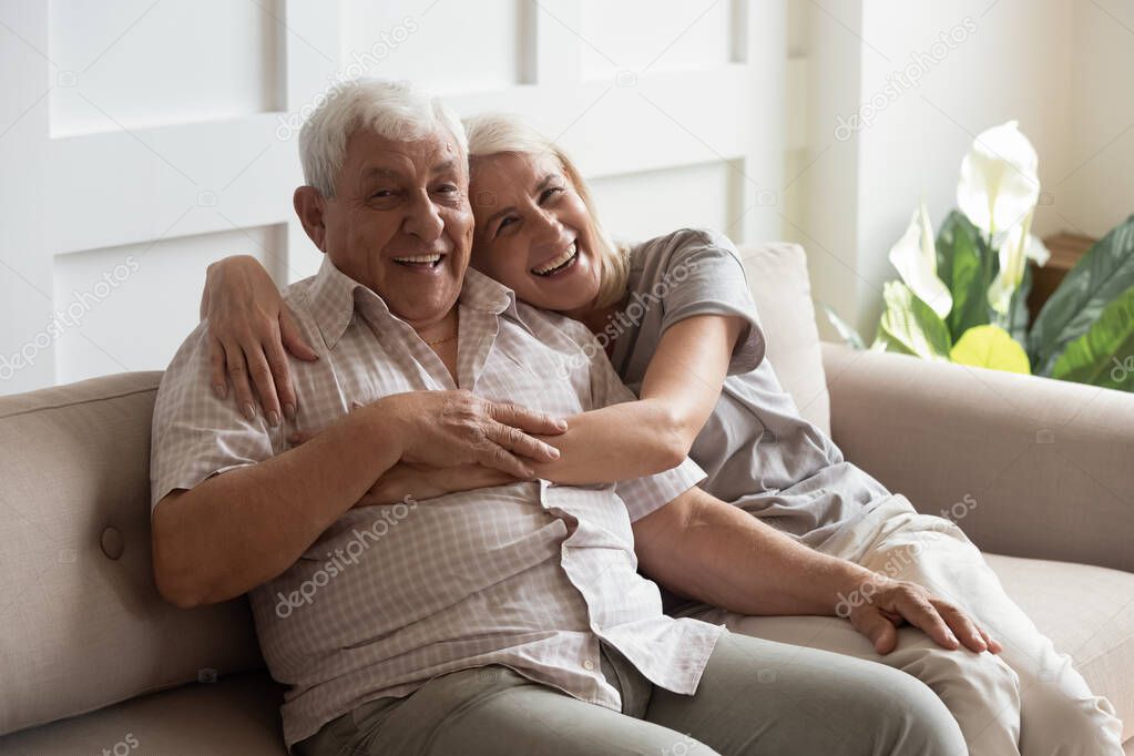 Happy mature couple resting on couch looking at camera