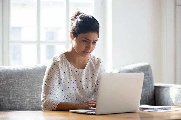 Focused Indian woman using laptop at home, looking at screen — Stock Photo, Image