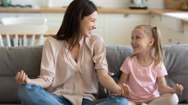 Mutlu anne ve küçük kız nilüfer çiçeği pozunda oturuyorlar.