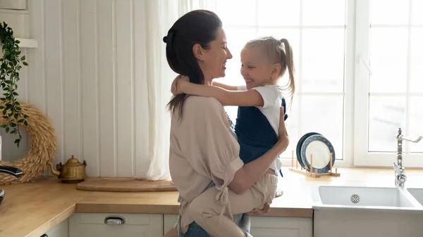 Happy mother holding little daughter, hugging, standing in kitchen — Stock Photo, Image