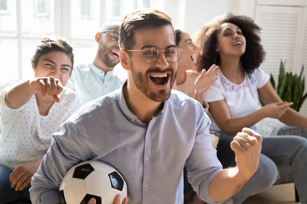 Excited man celebrating goal, watching football with diverse friends