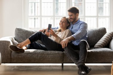 Mutlu çift kanepede birlikte rahatlıyor, cep telefonu kullanıyor.