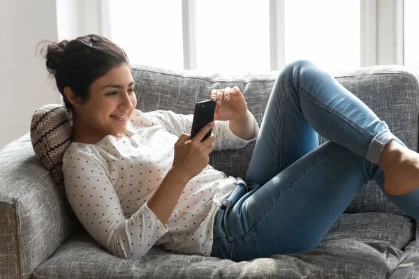 Mulher indiana feliz relaxando no sofá em casa, usando o telefone — Fotografia de Stock