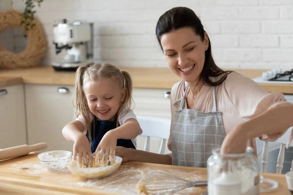 La piccola figlia aiuta la madre sorridente a impastare la pasta in cucina — Foto Stock