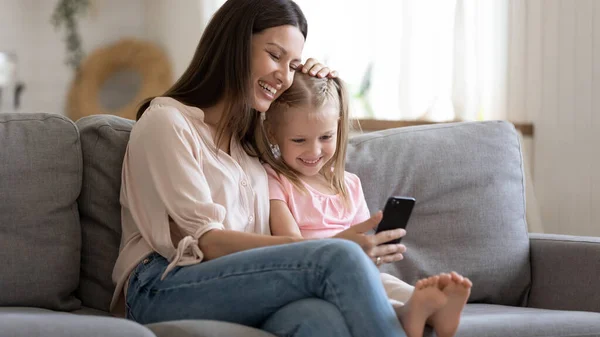 Mãe feliz e pequena filha olhando para a tela do telefone juntos — Fotografia de Stock