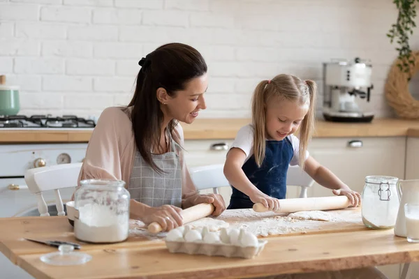 Glückliche Mutter und kleine Tochter rollen gemeinsam Teig aus — Stockfoto