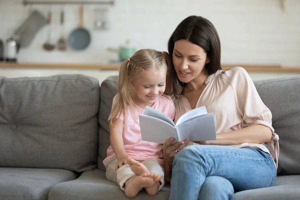 Mãe feliz e filhinha lendo livro juntos em casa — Fotografia de Stock