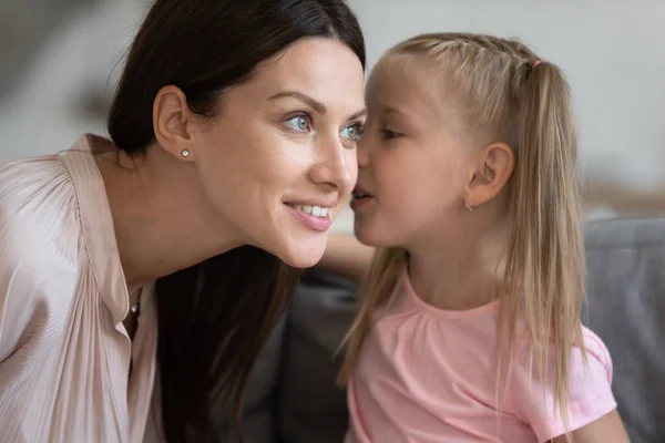 Маленькая дочь рассказывает секрет улыбающейся матери, шепчет на ухо — стоковое фото