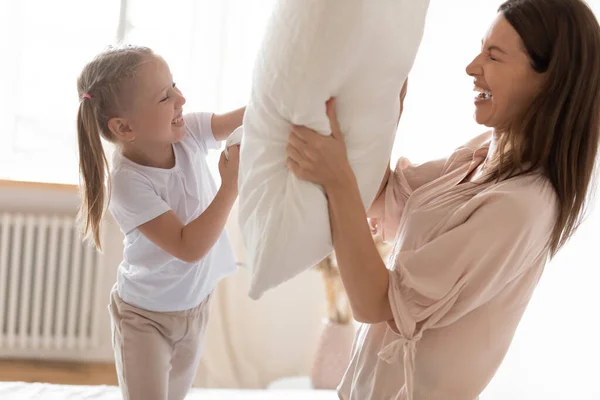 Emocionados madre e hija pequeña jugando pelea de almohadas de cerca —  Fotos de Stock