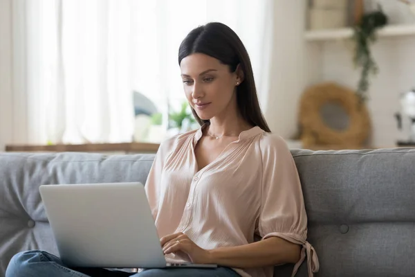 Ernstige jonge vrouw met behulp van laptop thuis, op zoek naar scherm — Stockfoto