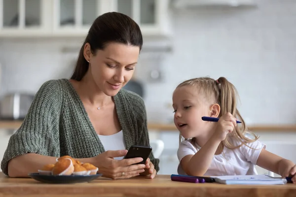 Little daughter distracted from drawing, looking at phone with mother — Stock Photo, Image