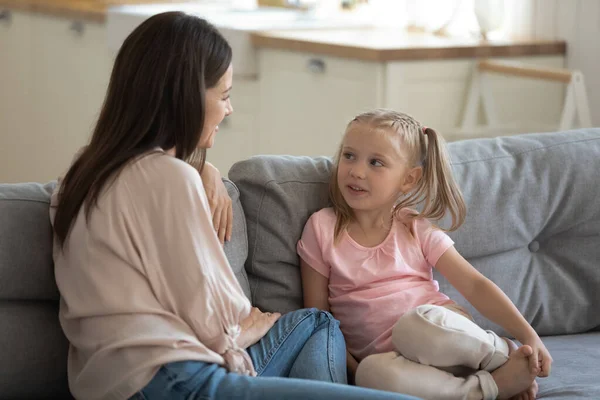 Madre feliz e hija pequeña hablando, sentados en el sofá — Foto de Stock