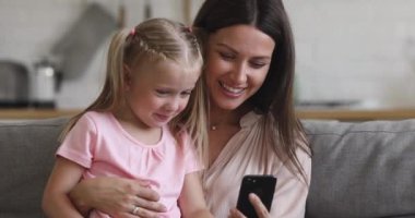 Mutlu anne küçük kızı kucaklıyor. Kanepeye oturup telefonla konuşuyor.