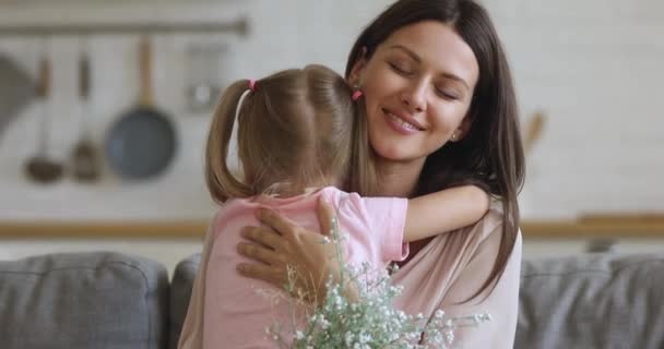 Щаслива вдячна молода мама обіймає дочку, яка тримає букет квітів — стокове відео