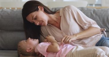 Mutlu anne kızıyla oynuyor rahat bir kanepede yatıyor.