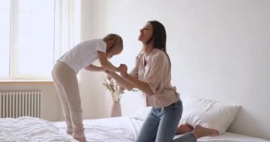 Happy mother and child girl holding hands jumping on bed