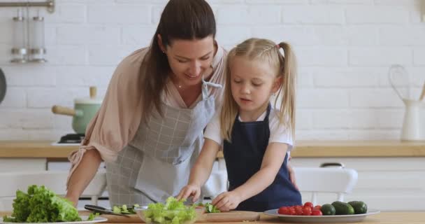 Kid daughter learning cooking helping mom cut vegetable salad — Stockvideo