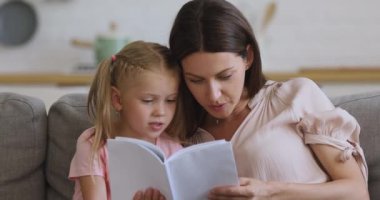 Mutlu aile annesi ve küçük kızı evde kitap okuyor.