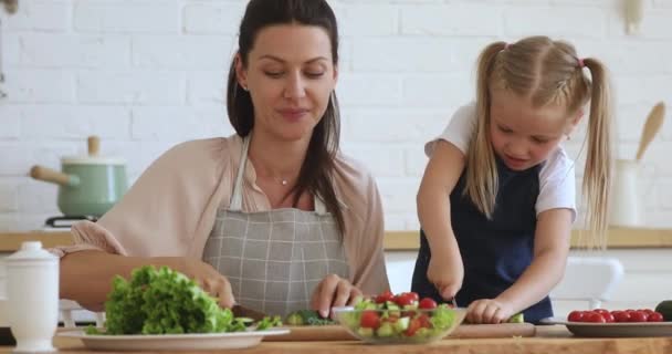 Genç anne, kızına mutfakta taze salata kesmeyi öğretiyor. — Stok video