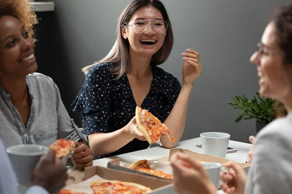 Asian employee eat pizza seated with mates at lunch break