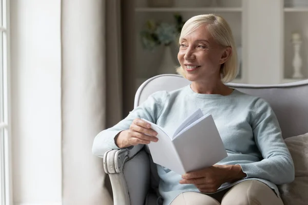 Distraído de la lectura feliz señora madura mirando por la ventana . —  Fotos de Stock