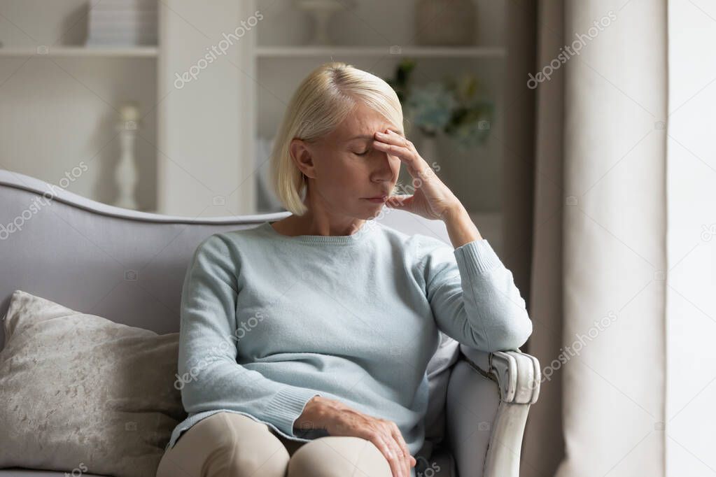 Exhausted mature lady suffering from head ache at home.