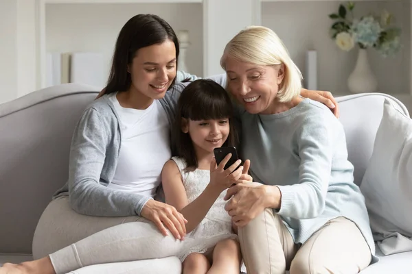 Adorable chica mostrando videos en el teléfono celular a mamá y la abuela . —  Fotos de Stock