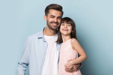 Gülümseyen genç baba ve anaokulu kızı birlikte poz vererek sarılıyorlar.