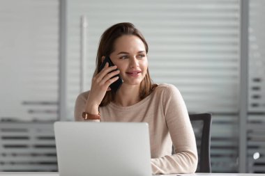 Gülümseyen iş kadını telefonla konuşuyor, laptop kullanıyor, iş görüşmesi yapıyor.