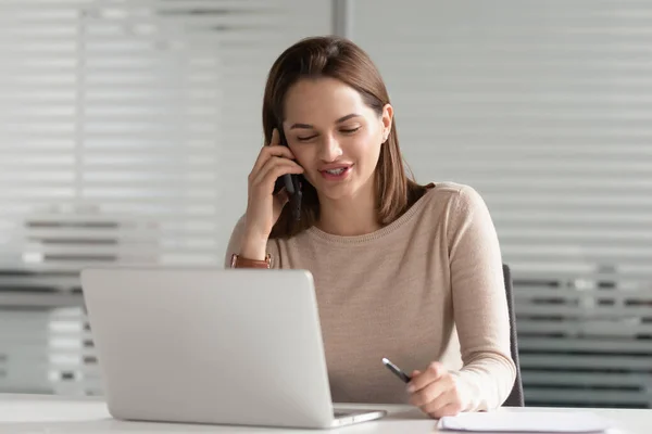 Femme d'affaires occupée parlant au téléphone, utilisant un ordinateur portable, assise au bureau — Photo