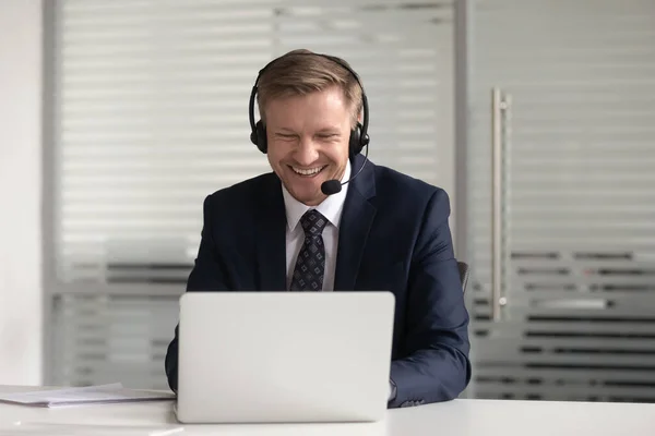 快乐微笑的商人在耳机里使用笔记本电脑，在网上工作 — 图库照片