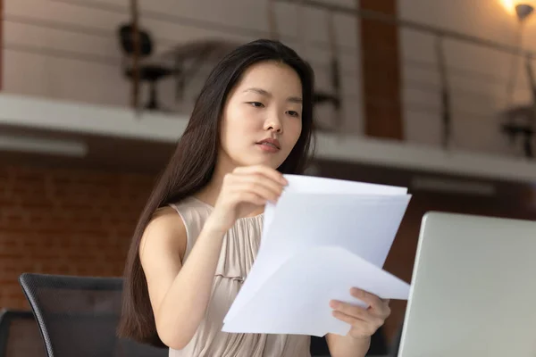 Zaměřený mladý asijské businesswoman čtení dokumentů, pomocí notebooku — Stock fotografie