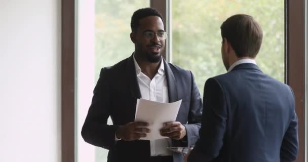 Twee gelukkige diverse zakenmannen praten lachen hand schudden staande in het kantoor — Stockvideo