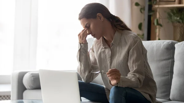 Moe jonge vrouw die een bril vasthoudt, heeft last van haar ogen na het computerwerk. — Stockfoto