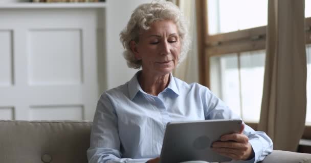 Felice donna anziana in possesso utilizzando tablet digitale rilassarsi sul divano — Video Stock