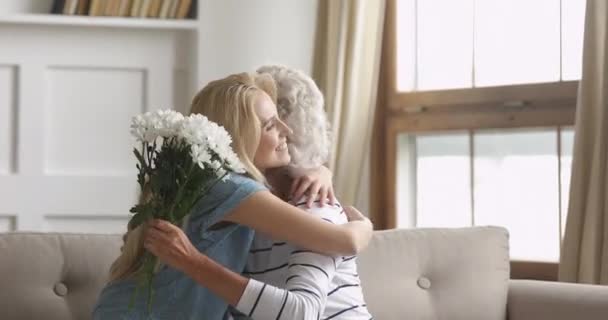 Figlia adulta che presenta fiori congratulandosi abbracciando la vecchia madre, ritratto — Video Stock