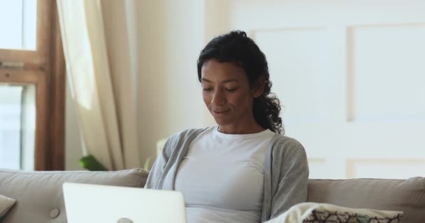 Gelukkig jong Afrikaans amerikaans vrouw met behulp van laptop zitten op bank — Stockvideo