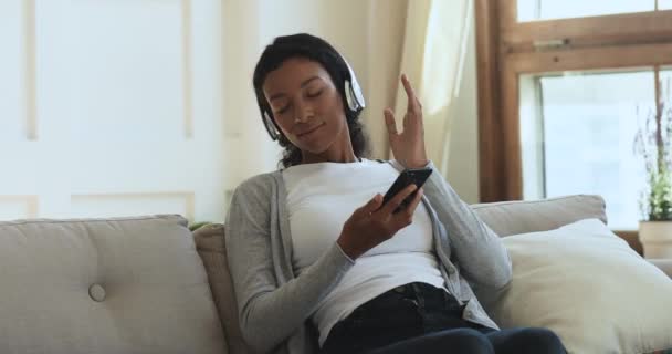 Mulher africana relaxada usando fones de ouvido sem fio ouvindo música móvel — Vídeo de Stock